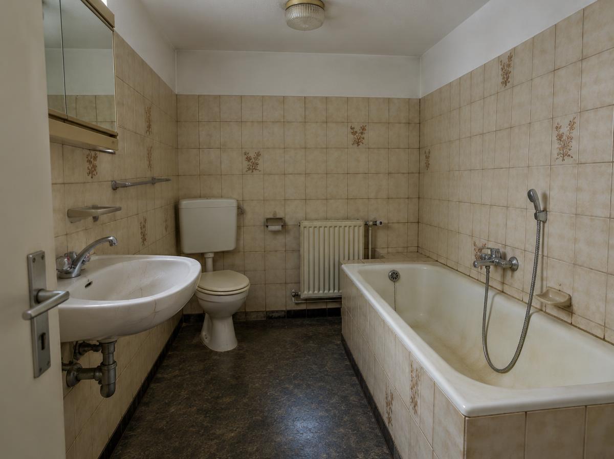 Älteres Bad mit vergilbter Badewanne, beige Fliesen und dunklem Boden